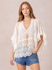Model poses in a white lace V-neck cover-up with a relaxed silhouette, sheer long sleeves, layered ruffle cuffs, and an intricate lace hem.