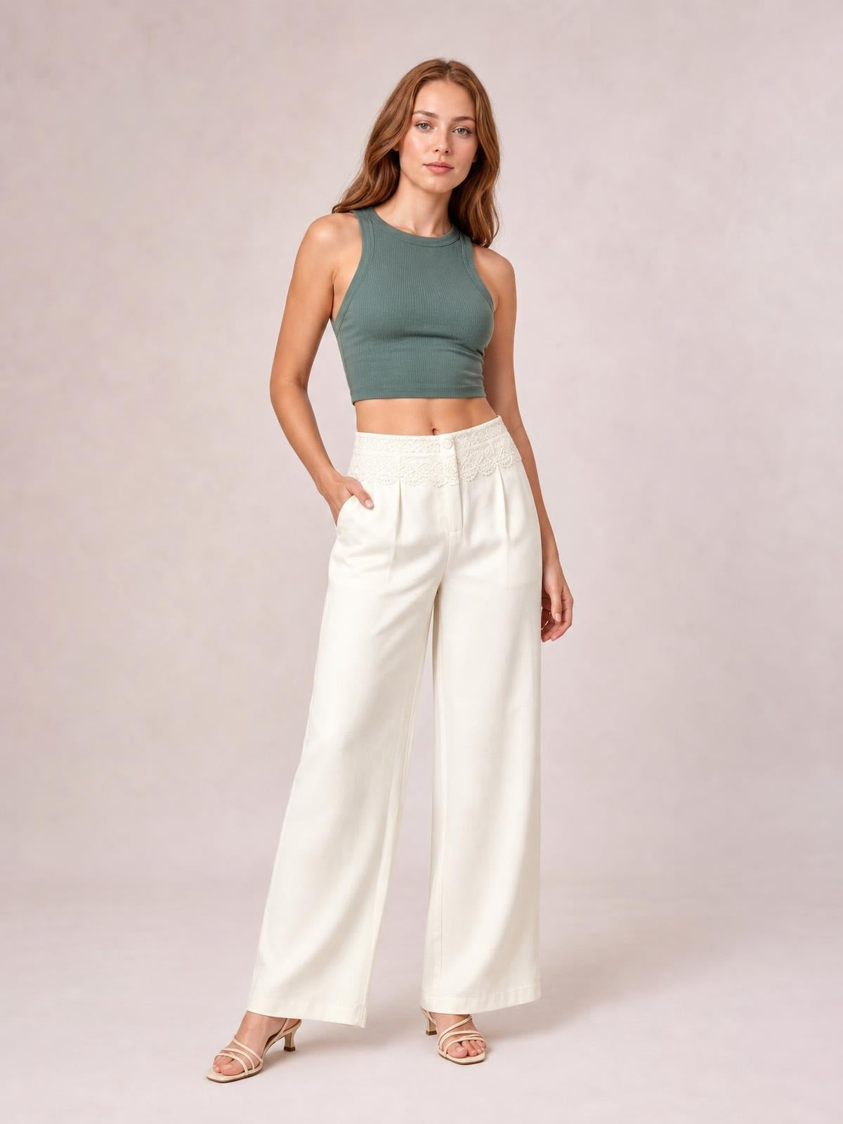 A model poses in cream wide-leg pants with a lace-trimmed waist, front pleats, button closure, and side pockets.
