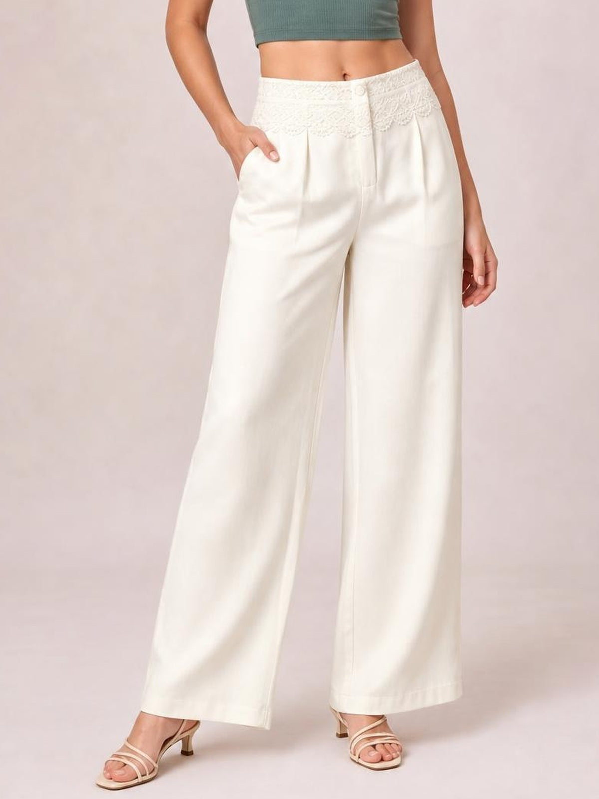 Model wearing ivory lace-waist wide-leg pants with front pleats and pockets, posed with one hand tucked into a pocket.