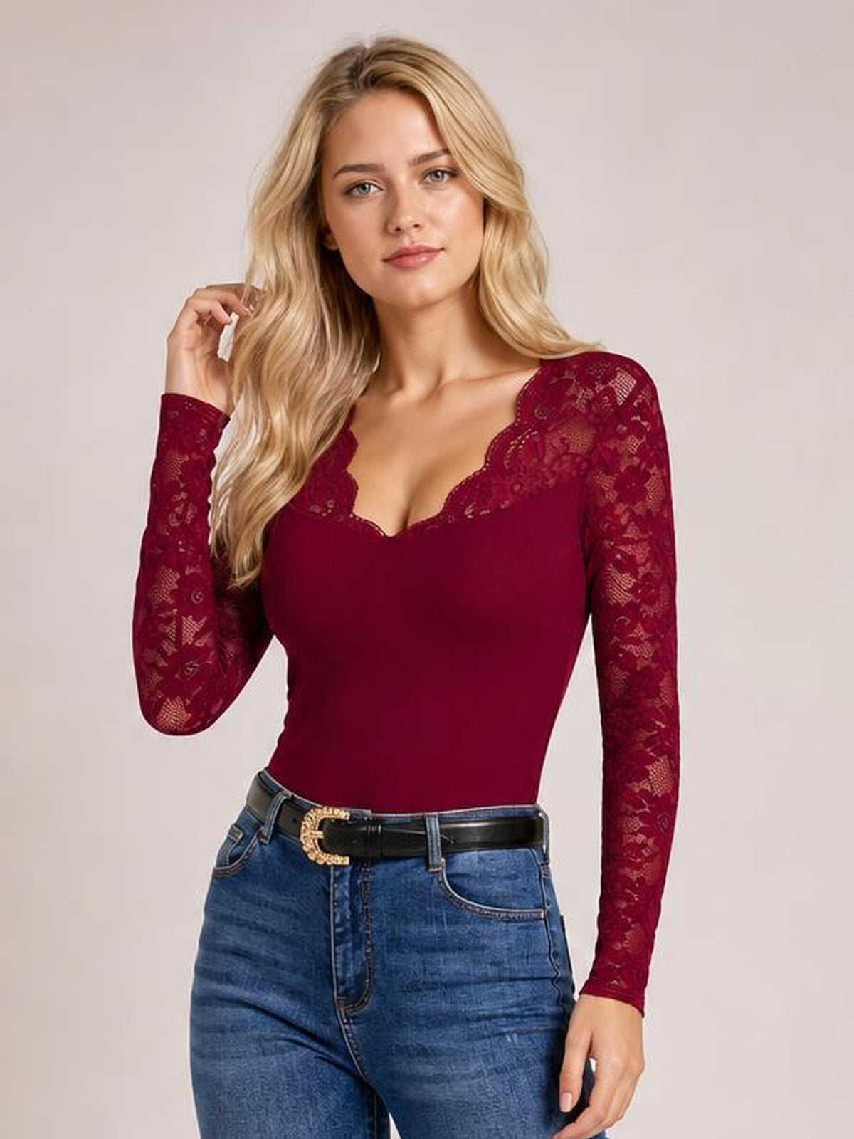 A model poses with one hand in her hair wearing a burgundy lace V-neck long-sleeve top with sheer floral sleeves and a fitted silhouette.