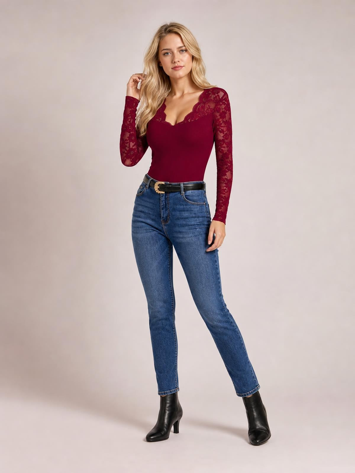 Model wears a burgundy lace V-neck long-sleeve top with semi-sheer floral sleeves and a fitted silhouette, posing with one hand in her hair.