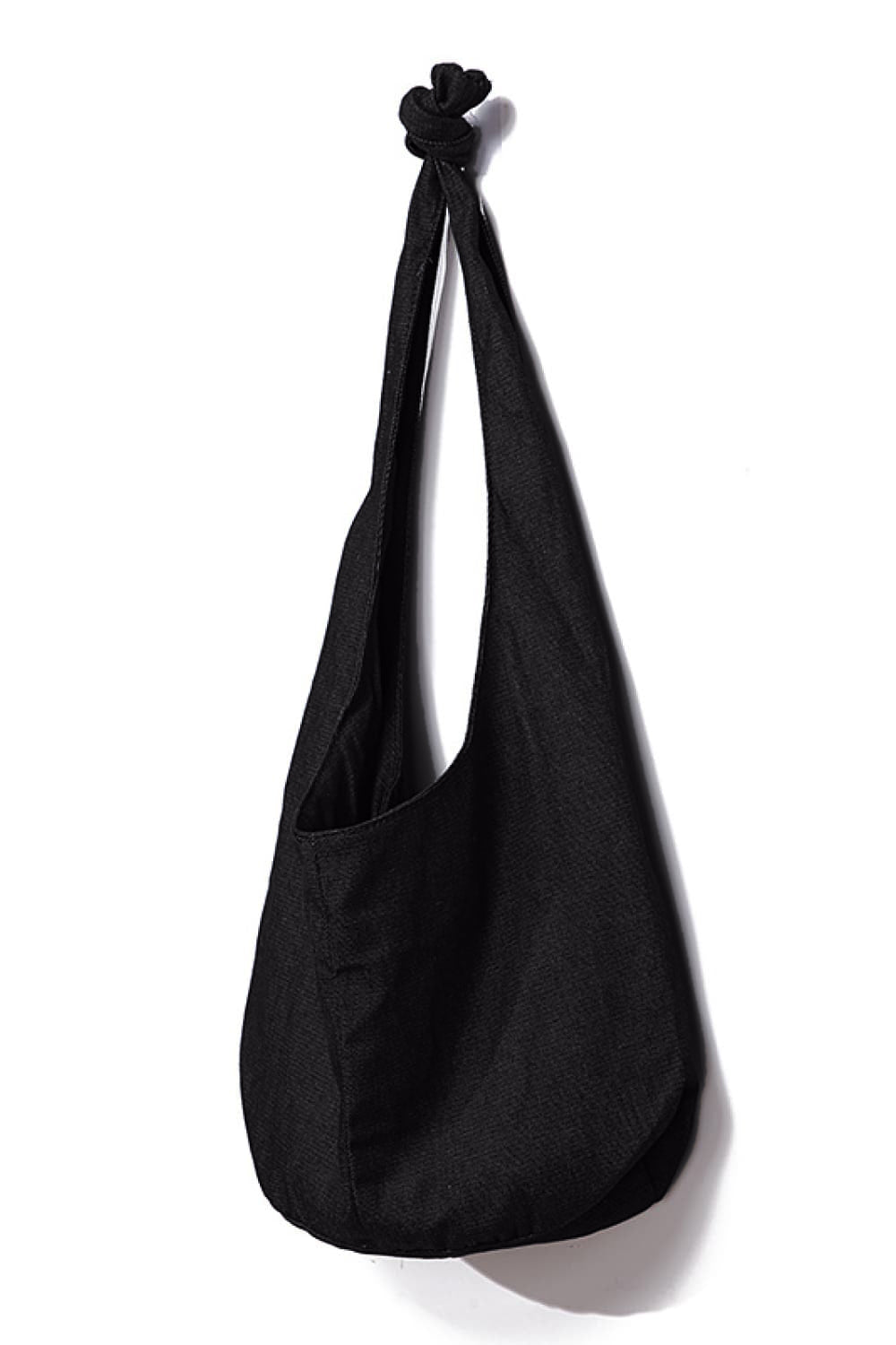 Large black canvas crossbody bag with a softly rounded, slouchy silhouette, open top, elongated strap, and gathered knot detail at the top.