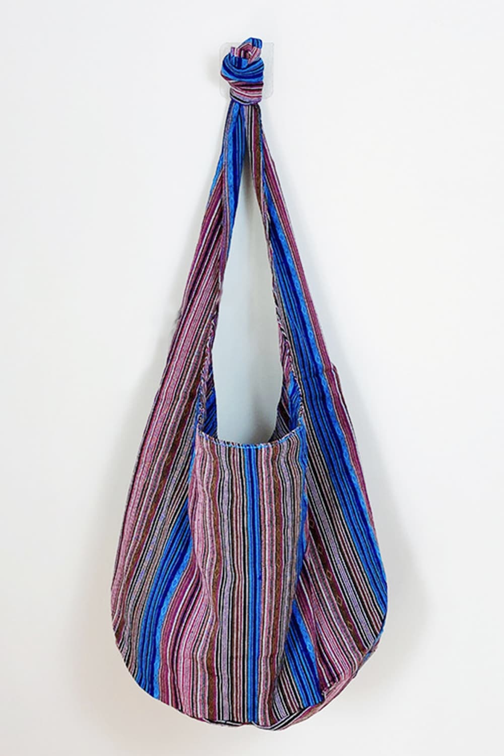 Large striped canvas crossbody bag in blue, pink, and black with a softly rounded silhouette, long draped strap, and gathered knot at the top.