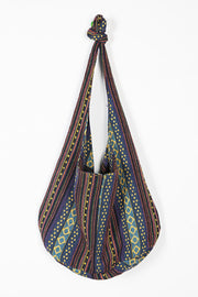 Large canvas crossbody bag with multicolored geometric stripes, a softly rounded slouchy silhouette, and an elongated strap gathered into a top knot.