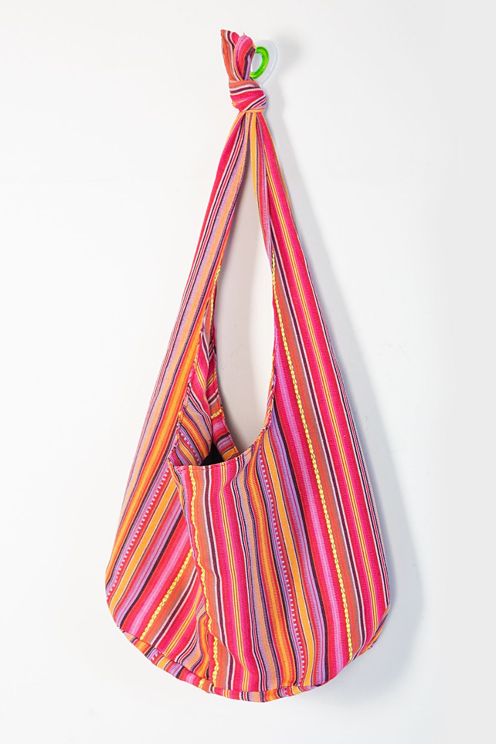 A large canvas crossbody bag in vivid multicolor stripes features a softly rounded silhouette, open top, elongated strap, and gathered knotted detail.