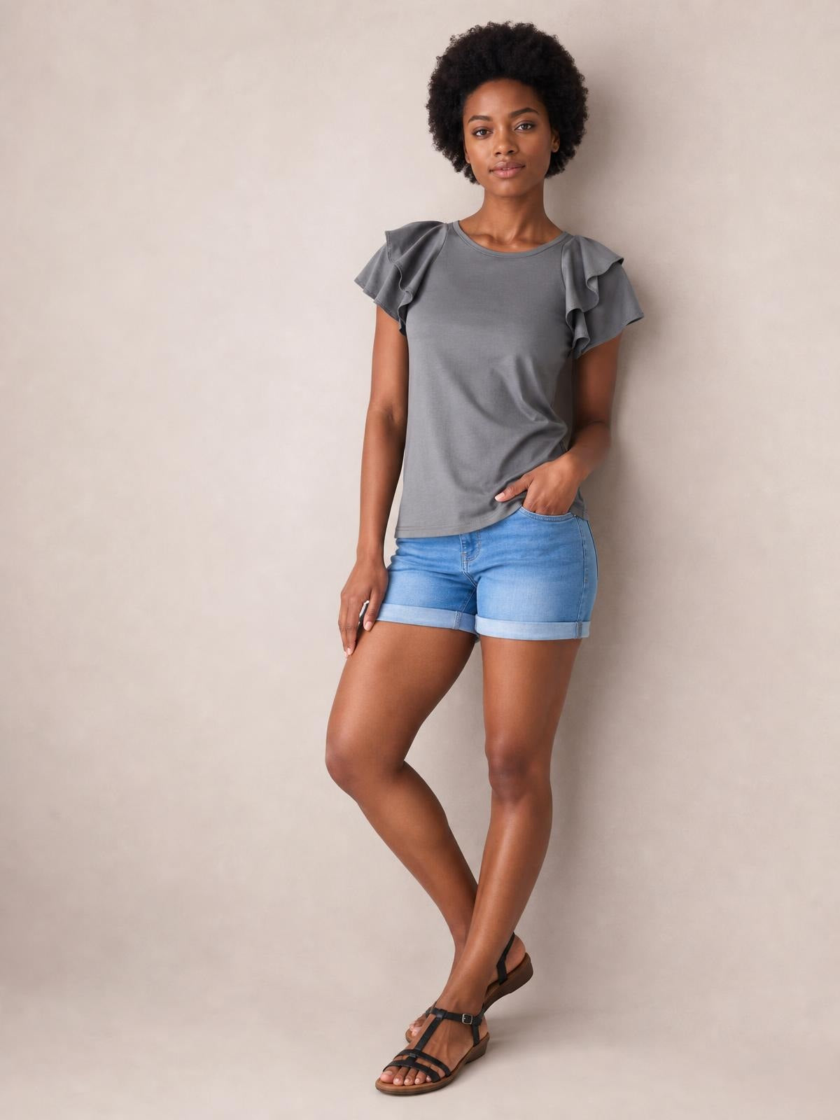 Model wearing a solid gray layered flutter sleeve round neck top with a relaxed regular-length silhouette, standing with one hand in her pocket.