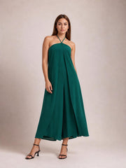 Model standing in a deep green layered halter neck jumpsuit with a flowing wide-leg silhouette and draped front overlay.