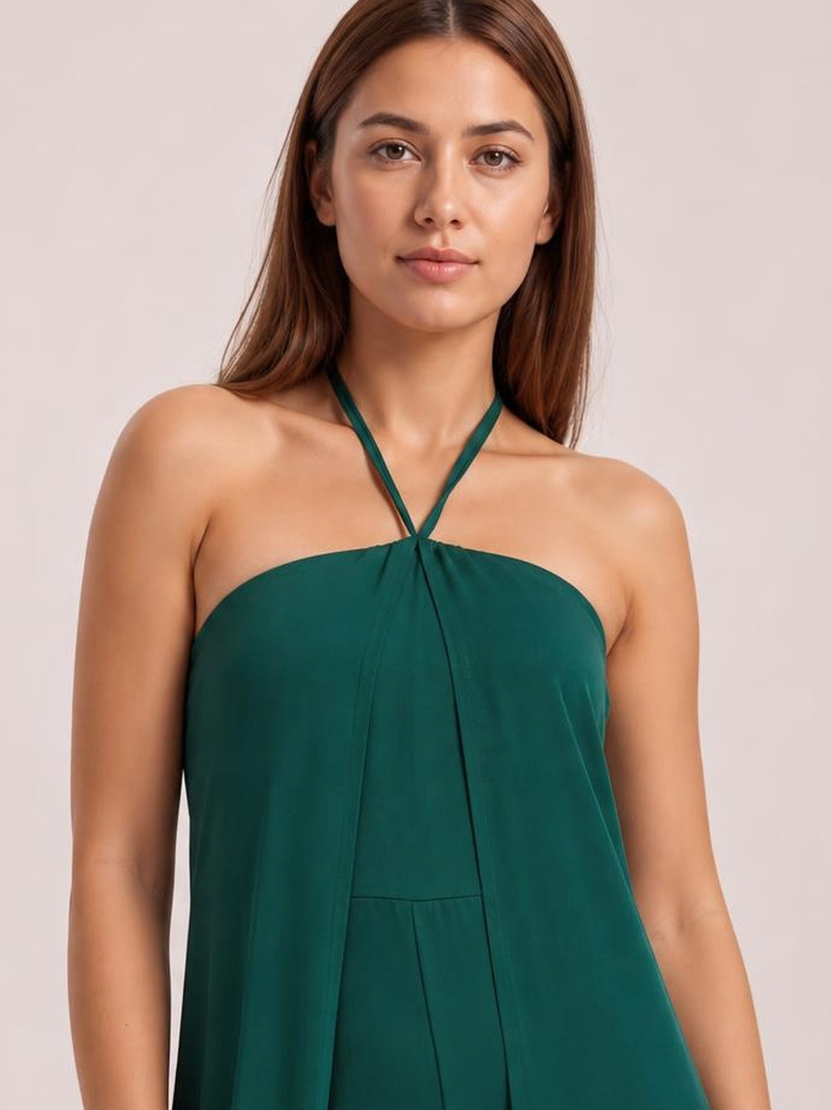 A model faces forward in a deep green layered halter neck jumpsuit with a flowing, wide-leg silhouette and gathered center-front construction.