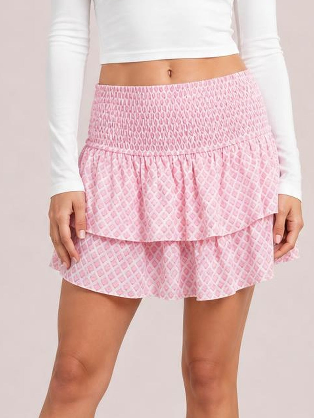 Model holds the hem of a pink patterned Layered Mini Skirt, showing its smocked ruched waistband and two ruffled tiers in a playful flared silhouette.