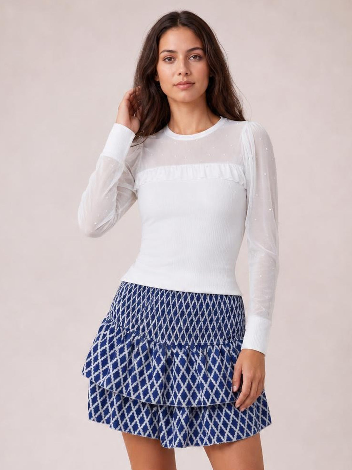 Model touching her hair wears a blue-and-white patterned layered mini skirt with a smocked waistband, tiered ruffles, and a playful flared silhouette.