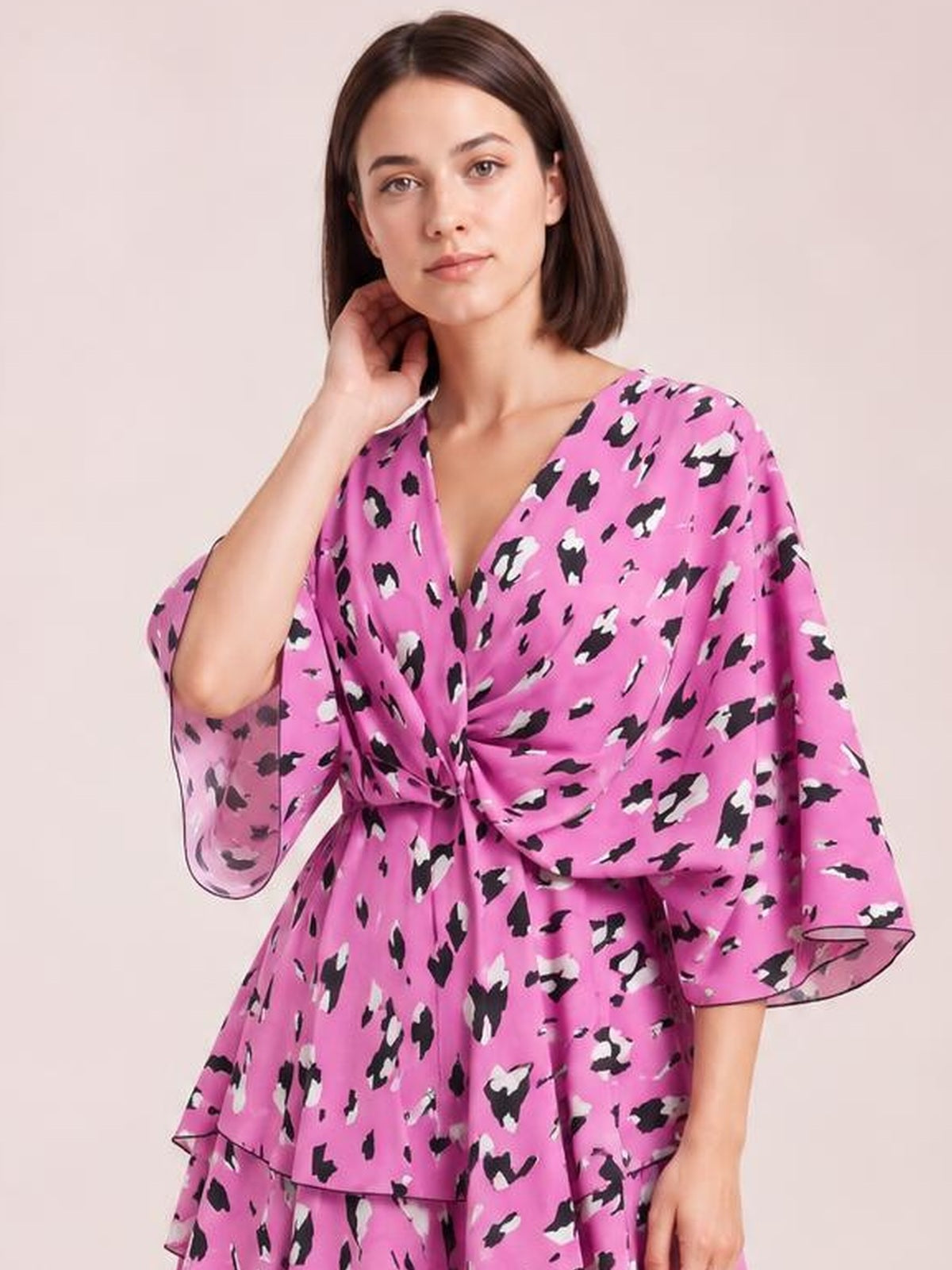 A model poses in a pink, black, and white printed surplice mini dress with ruched waist detailing, tiered construction, and flowing three-quarter sleeves.