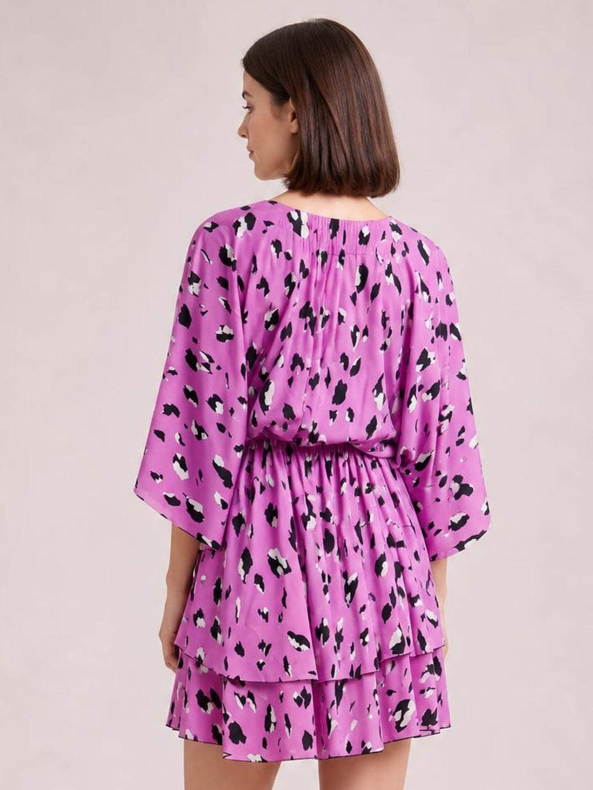 Model shown from behind in a pink, black, and white printed mini dress with long sleeves, a ruched waist, and layered tiered ruffle skirt.