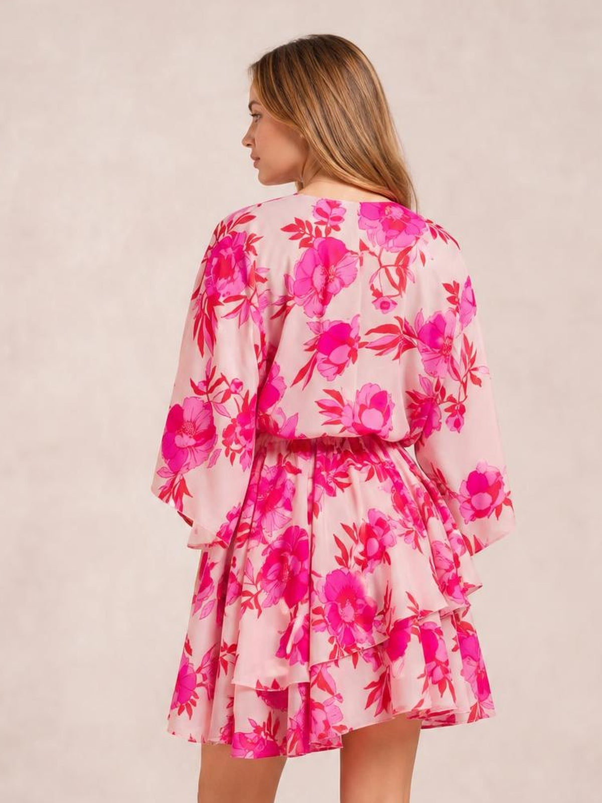 Model shown from the back in a pink floral printed mini dress with long sleeves, a cinched waist, ruched details, and layered tiered ruffles.