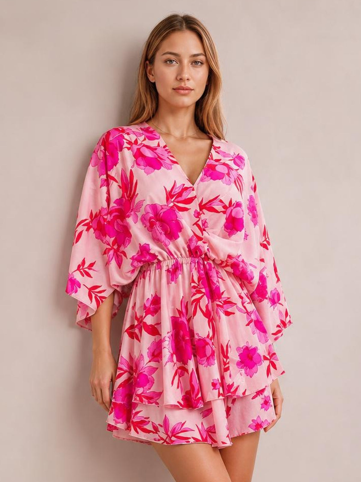A model wears a pink floral printed surplice mini dress with a V-neckline, ruched waist, flowing sleeves, and layered tiered ruffles.
