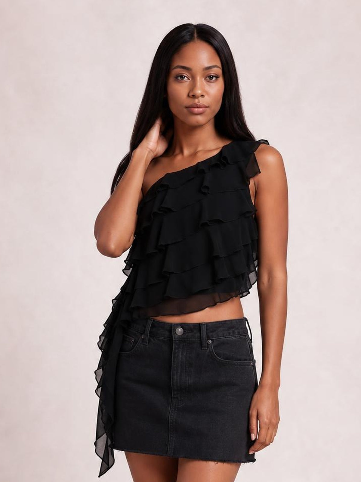 Model poses in a black one-shoulder tank with layered ruffled tiers, an asymmetrical cropped silhouette, and a dramatic cascading side detail.