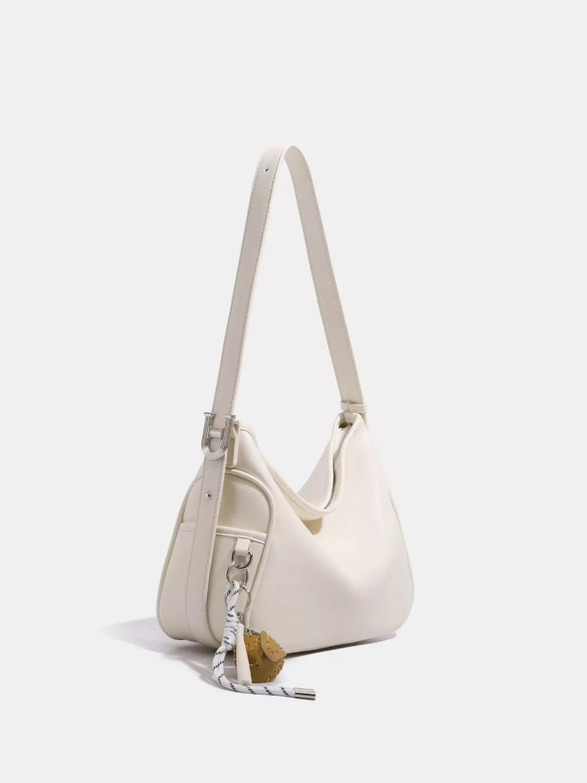 A medium ivory PU leather slouchy shoulder bag with a soft rounded silhouette, long adjustable strap, zip-top opening, silver-tone hardware, and a tassel charm.