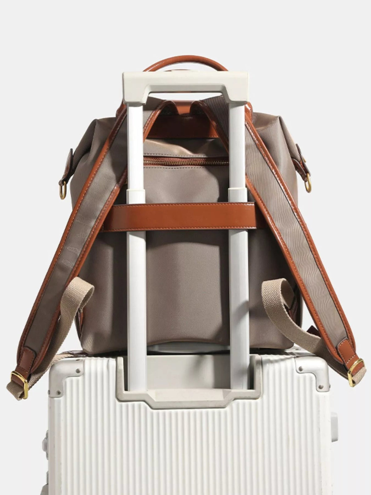 Medium taupe nylon backpack with brown faux leather trim, adjustable shoulder straps, top handle, front zip pocket, and luggage sleeve.
