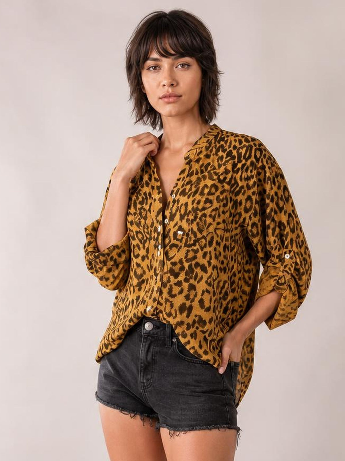 Model wearing a loose leopard-print blouse with a notched neckline, button front, and rolled long sleeves, paired with black denim shorts.