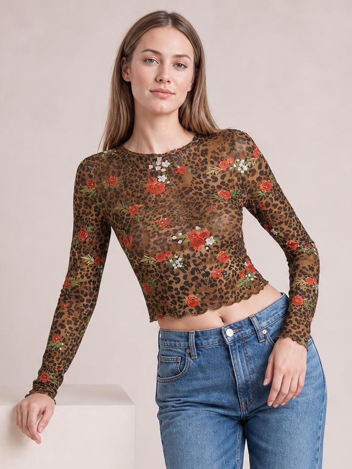 Model wearing a sheer leopard floral round neck long sleeve mesh T-shirt with a fitted silhouette and slightly scalloped hem, posing with one hand resting on a block.