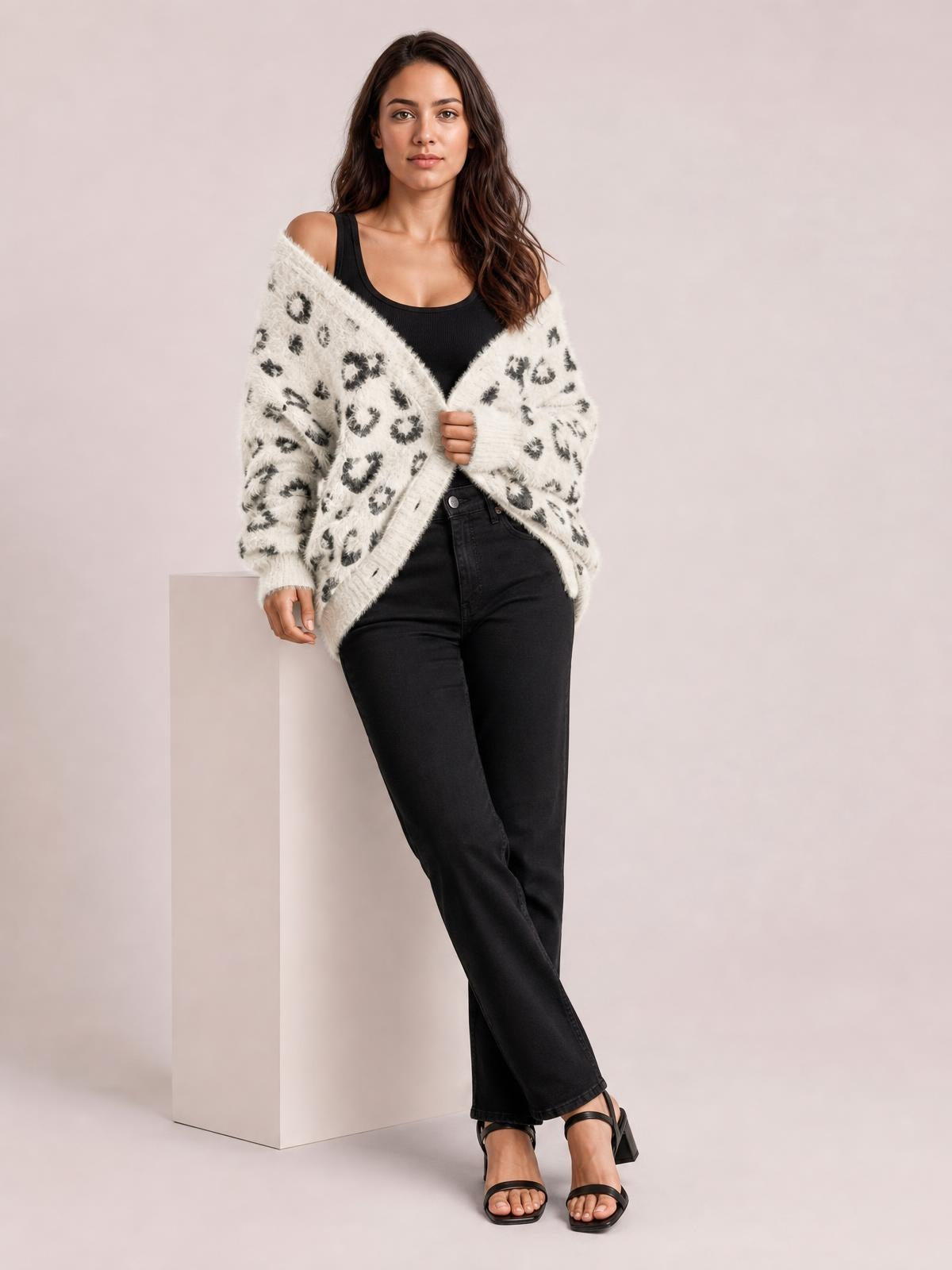 Model wears a cream leopard-print open-front cardigan with long sleeves and a relaxed silhouette, holding the front closed over a black top and jeans.