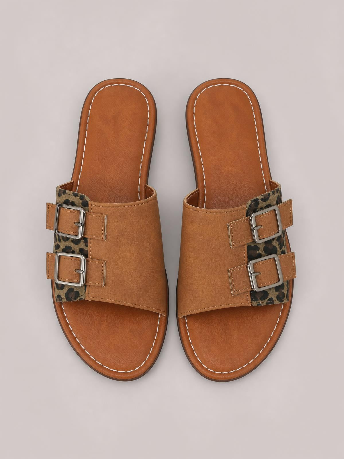 Tan leopard open toe flat sandals feature two adjustable silver buckles, wide PU leather straps, contrast stitching, and cushioned footbeds.