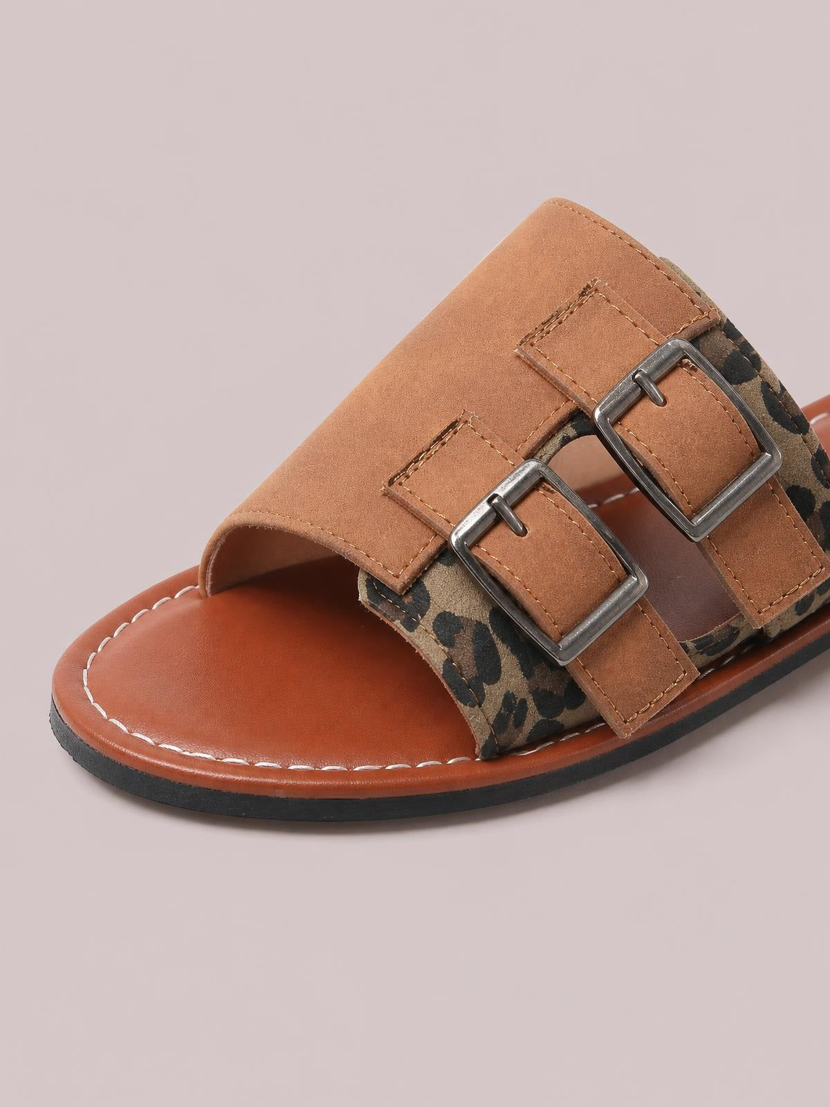 Close-up of leopard open toe flat sandals with tan PU leather straps, double metal buckles, a brown footbed, stitched trim, and a rubber sole.