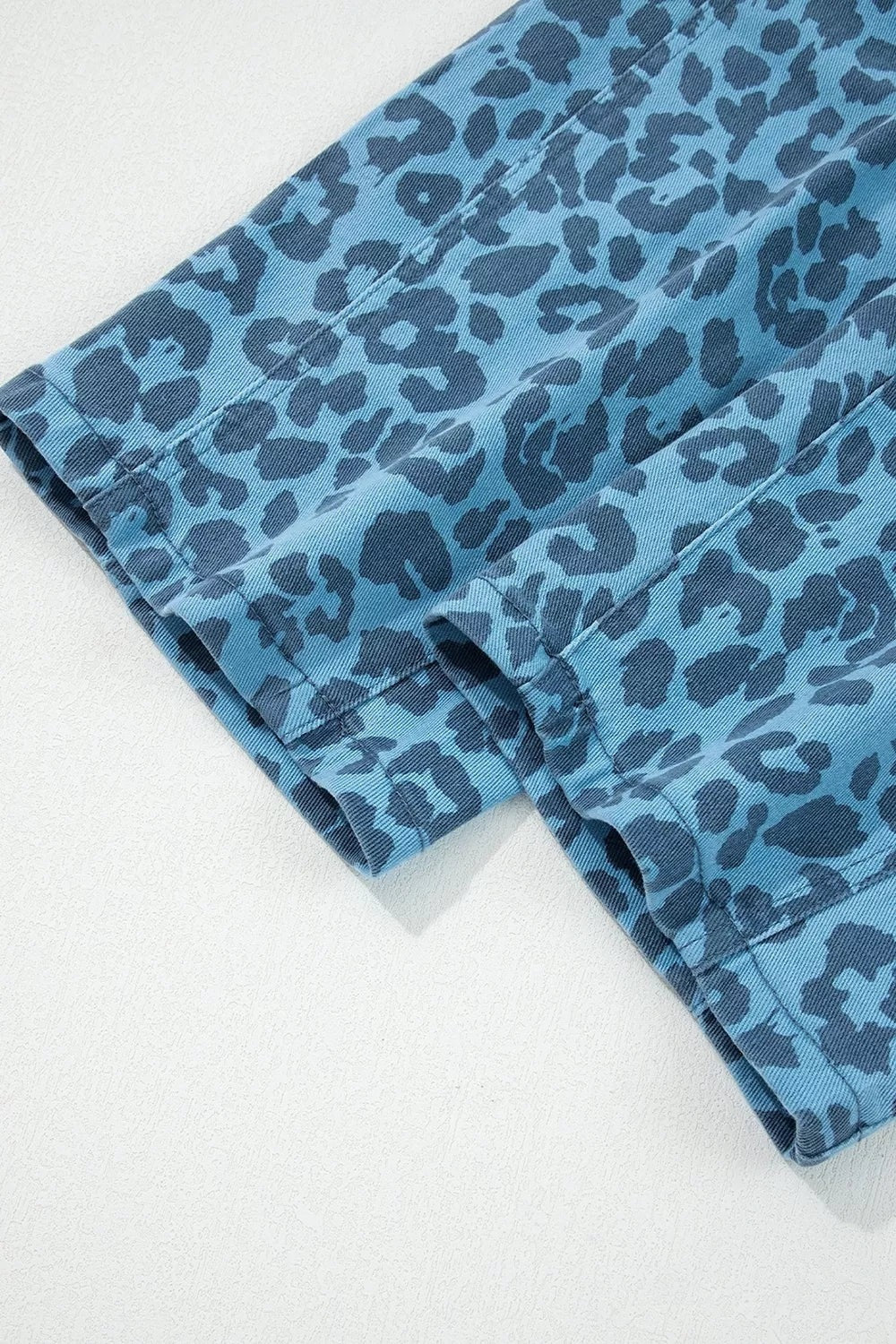 Blue leopard print barrel leg jeans shown folded, with wide legs, straight hems, and visible stitched panel seams highlighting their structured construction.