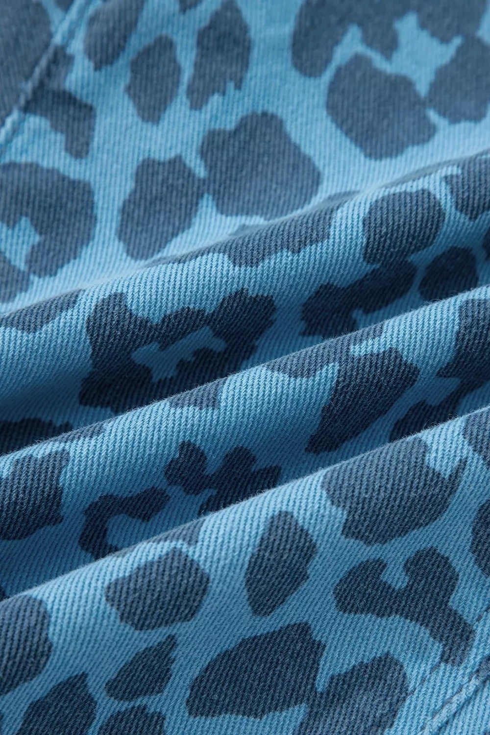 Close-up shows the blue denim fabric of leopard print barrel leg jeans, featuring a textured weave and contrasting dark leopard spots.