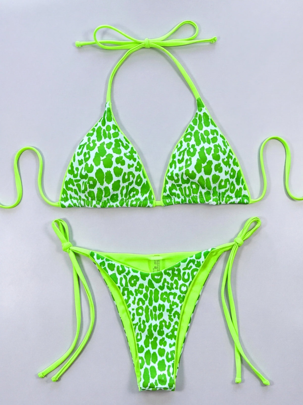 Green leopard print halter bikini set laid flat, featuring triangle cups, a skimpy tie-side bottom, and long adjustable neon-green string ties.