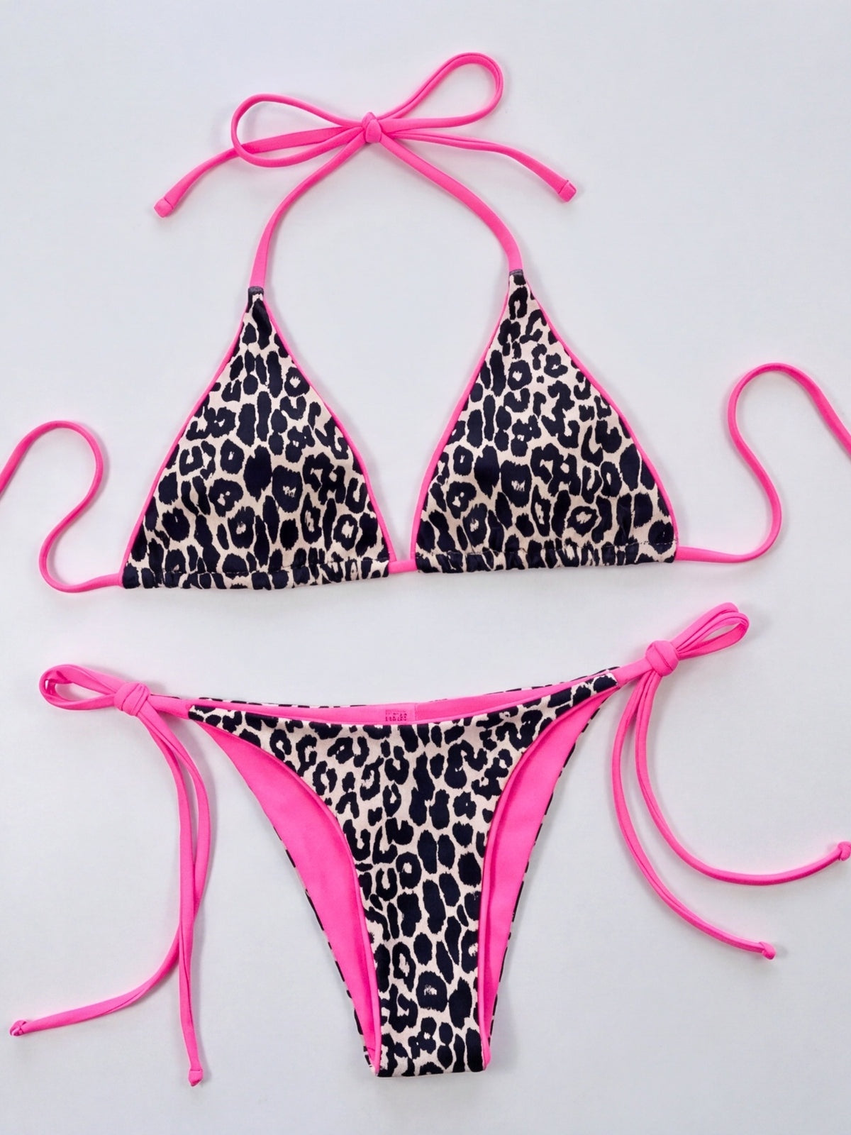 Leopard print halter-neck bikini set with triangular cups, vibrant pink trim, tie-side bottoms, and adjustable pink string ties shown in a flat lay.