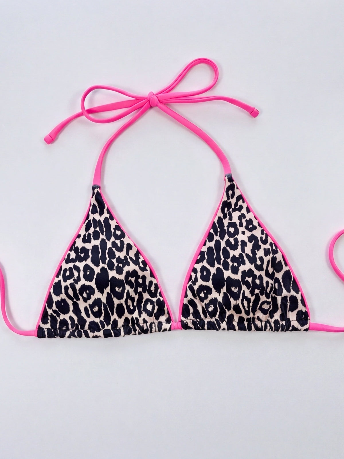 Leopard print bikini top laid flat, featuring a triangle halter neckline, bright pink trim, and long adjustable tie straps.
