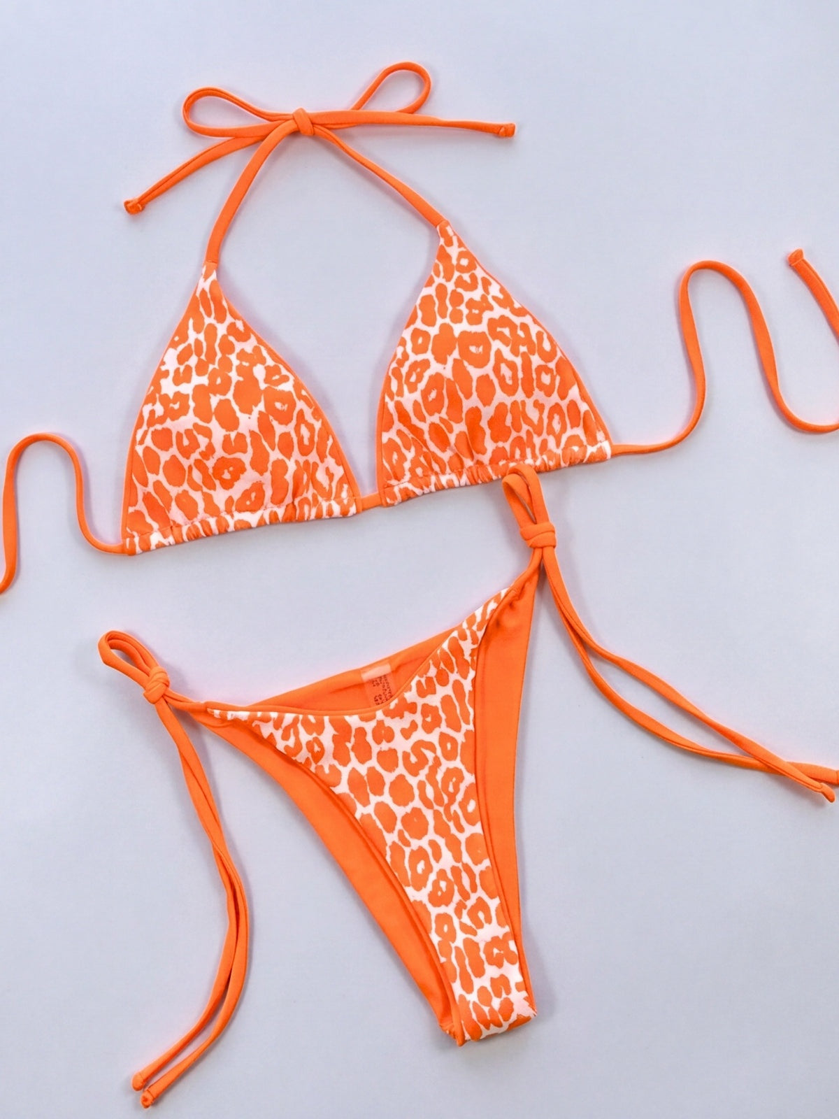 Orange and white leopard print halter neck bikini set displayed flat, featuring a triangle top and tie-side thong bottoms with adjustable string ties.