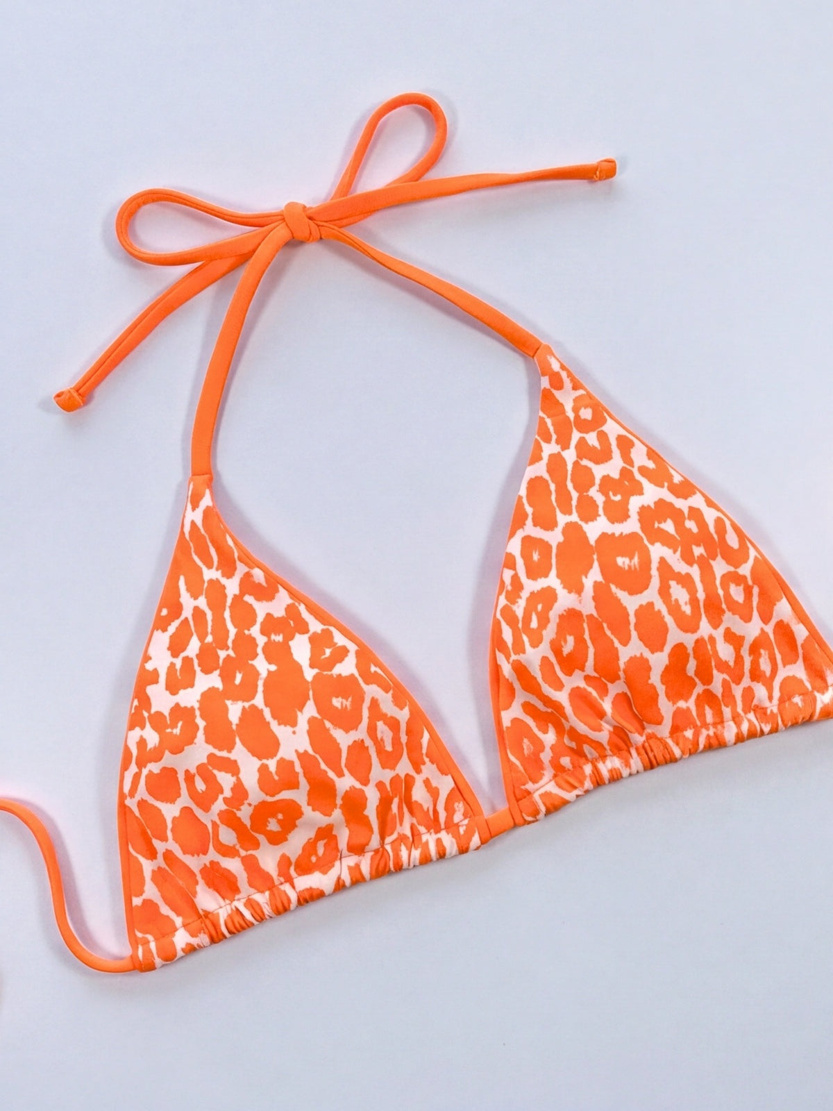 Orange leopard print bikini top laid flat, featuring a triangle silhouette, halter neck, long tie straps, and gathered underbust construction.