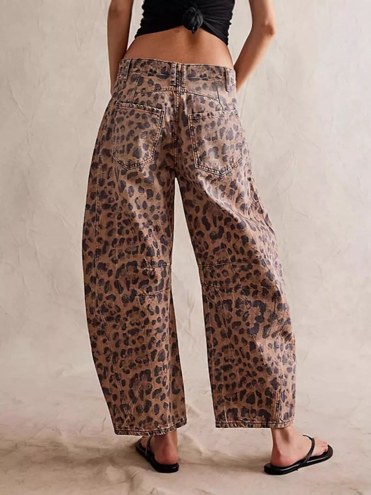 Model poses in leopard print wide leg jeans with a cropped ankle-length silhouette, belt loops, seam detailing, and two large back pockets.