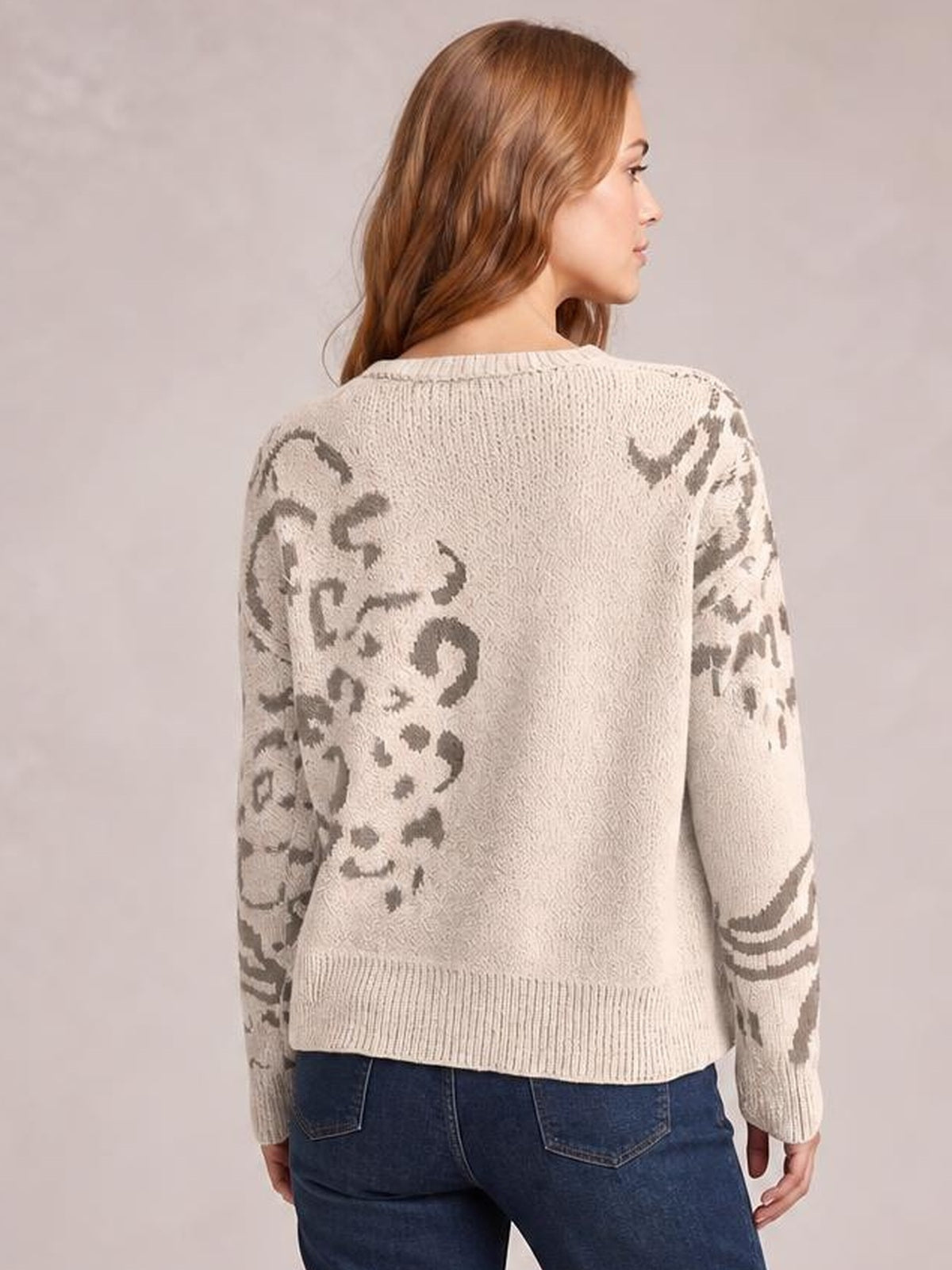 Model turned to show the back of a cream leopard relaxed fit sweater with gray spots, long sleeves, ribbed crew neckline, cuffs, and hem.