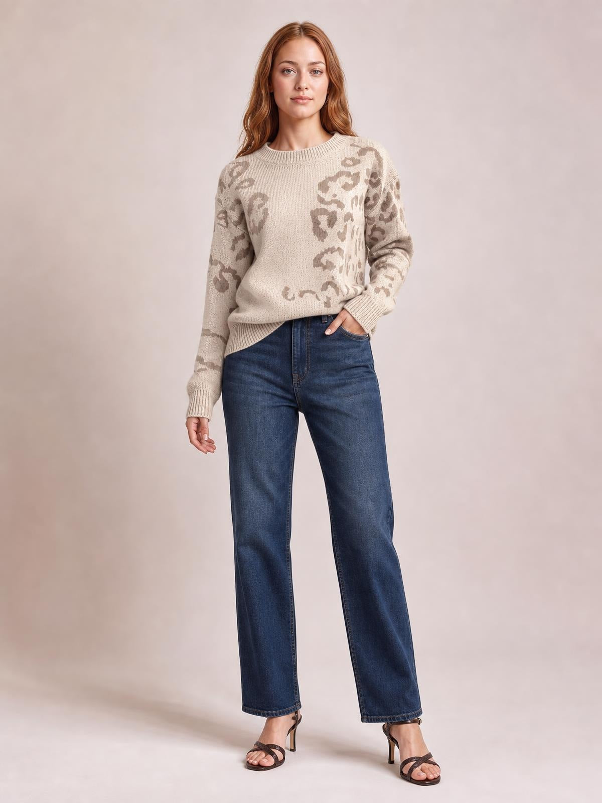 Model poses in a relaxed fit beige leopard print sweater with a ribbed crew neck, cuffs, and hem, paired with wide-leg jeans.