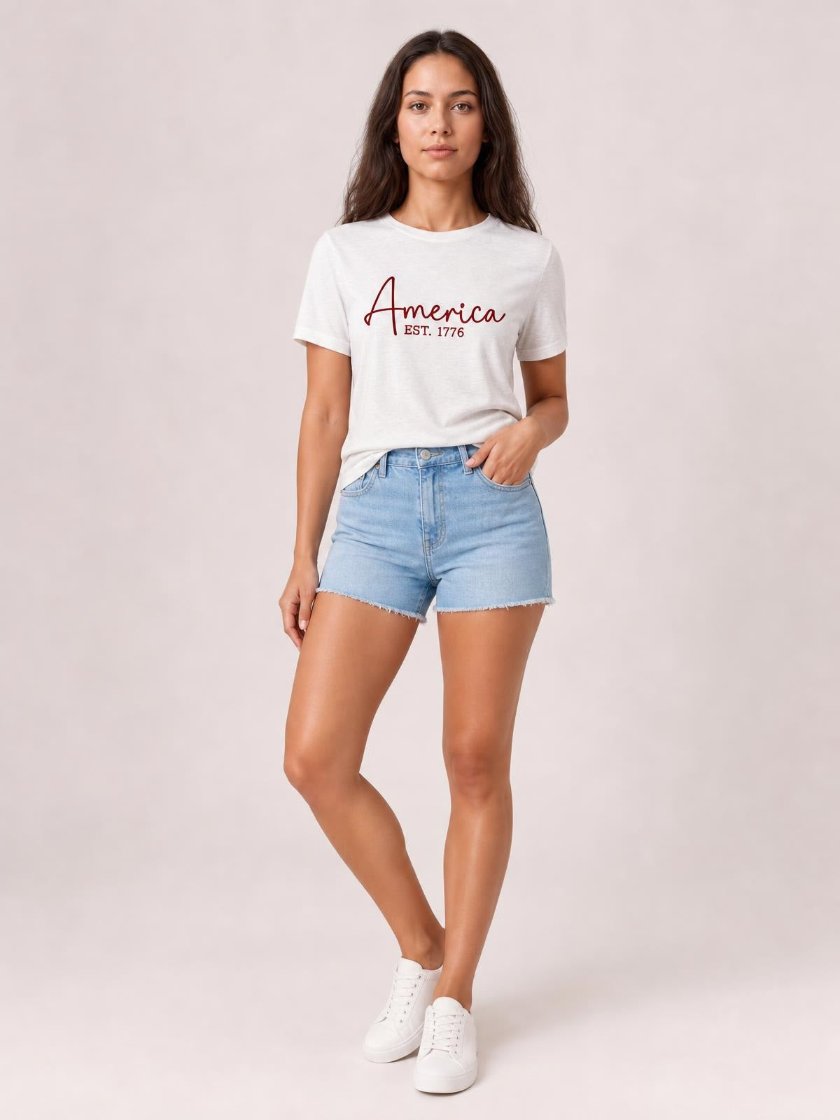 Model wears an opaque white round neck short sleeve T-shirt with an “America EST. 1776” letter graphic and a relaxed straight silhouette.