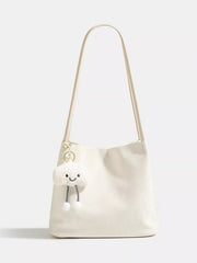 Cream medium PU leather shoulder bag with a long strap, softly structured silhouette, smooth construction, and a playful cloud charm with dangling pom-poms.
