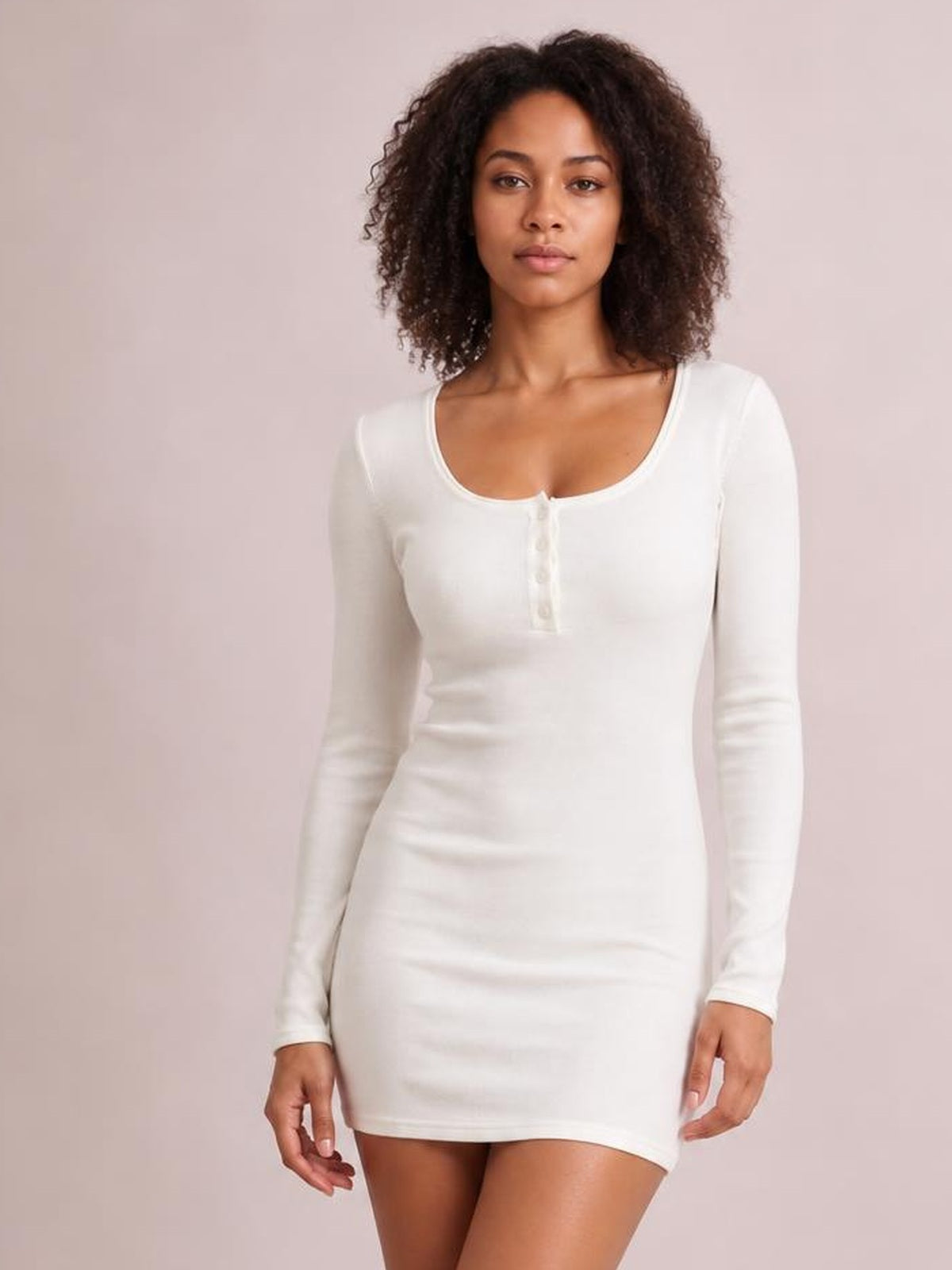 Model stands facing forward in a white long sleeve bodycon mini dress with a scoop neckline, stretchy fitted silhouette, and buttoned front placket.