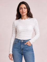Model stands in a white long sleeve jacquard slim top with a fitted silhouette, textured horizontal pattern, and scalloped neckline and cuffs.