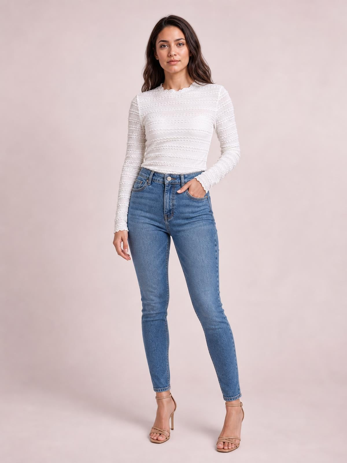 Model wears a white long-sleeve jacquard slim top with a fitted silhouette, textured horizontal pattern, and subtly scalloped neckline and cuffs, posing with one hand in a jeans pocket.