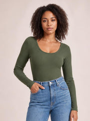 Model poses with one hand in her jeans pocket wearing an olive green long sleeve scoop neck T-shirt with a fitted silhouette and stretch construction.