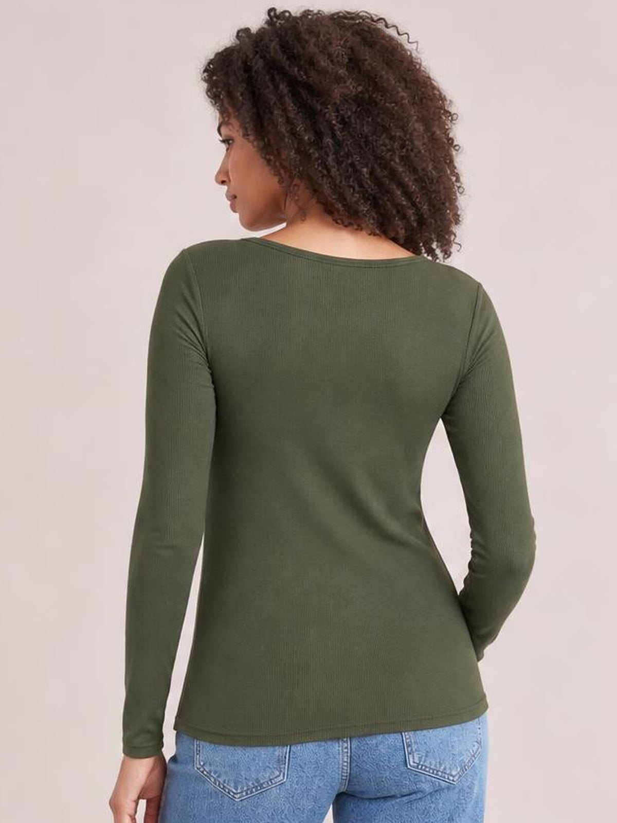 Model poses with her back to the camera in an olive green long sleeve scoop neck T-shirt with a fitted silhouette and stretch construction.
