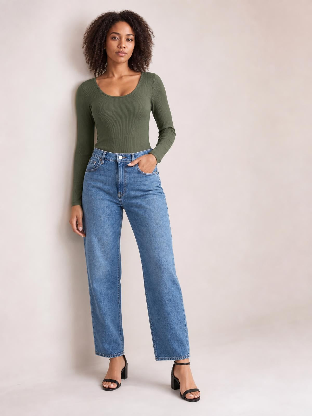Model wears an olive green long sleeve scoop neck T-shirt with a fitted silhouette and ribbed construction, paired with jeans, one hand in a pocket.
