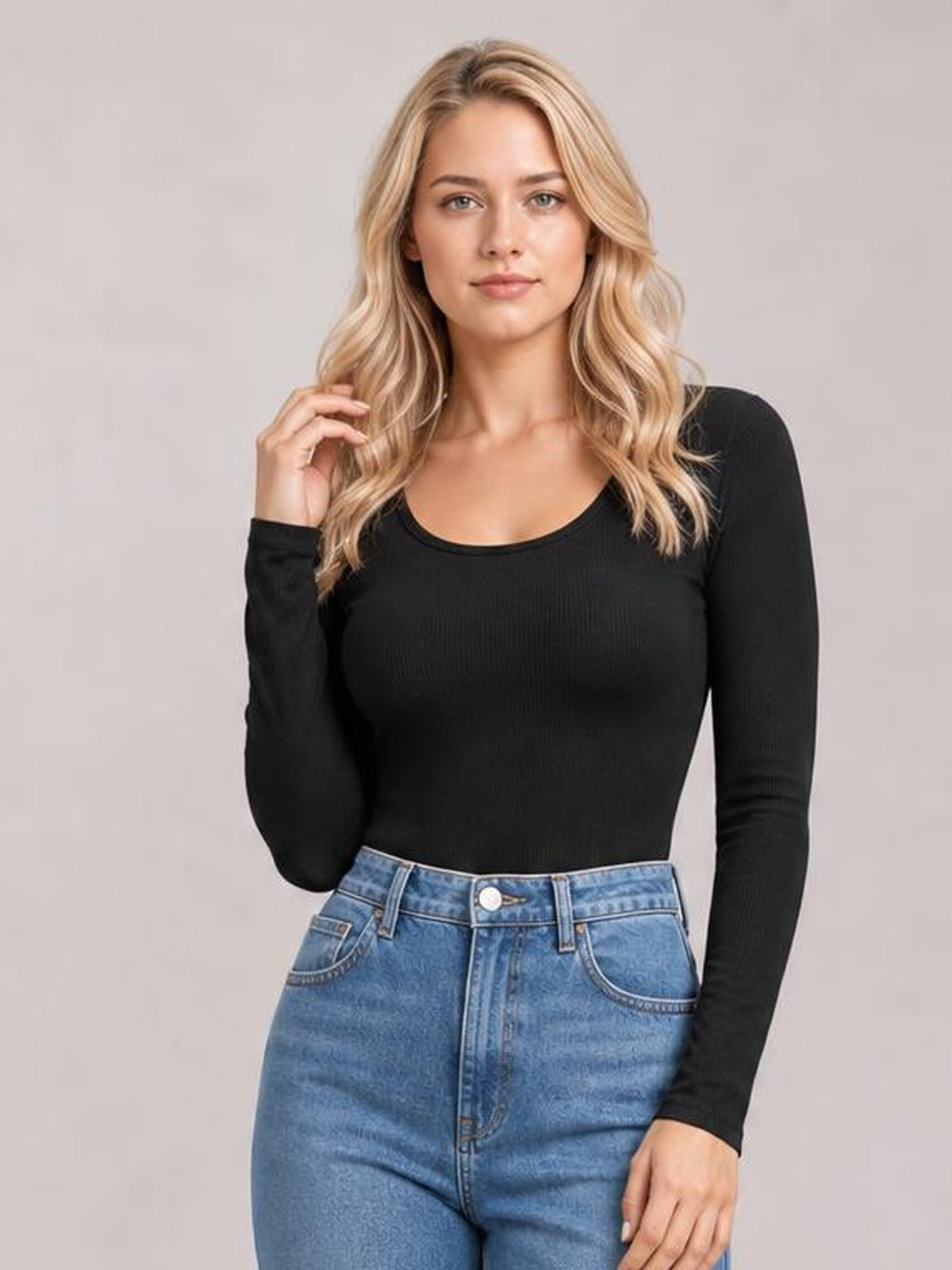 Model poses in a black long sleeve scoop neck T-shirt with a fitted silhouette and stretch construction, paired with high-waisted blue jeans.