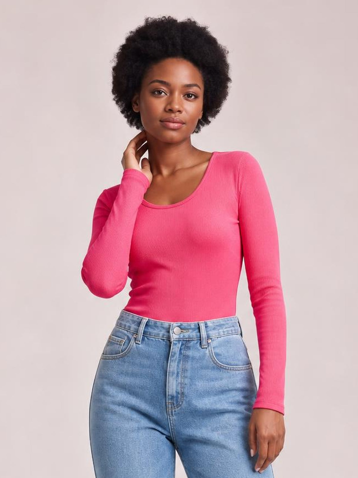 Model poses with one hand at her neck, wearing a bright pink long sleeve scoop neck T-shirt with a fitted silhouette and ribbed construction.