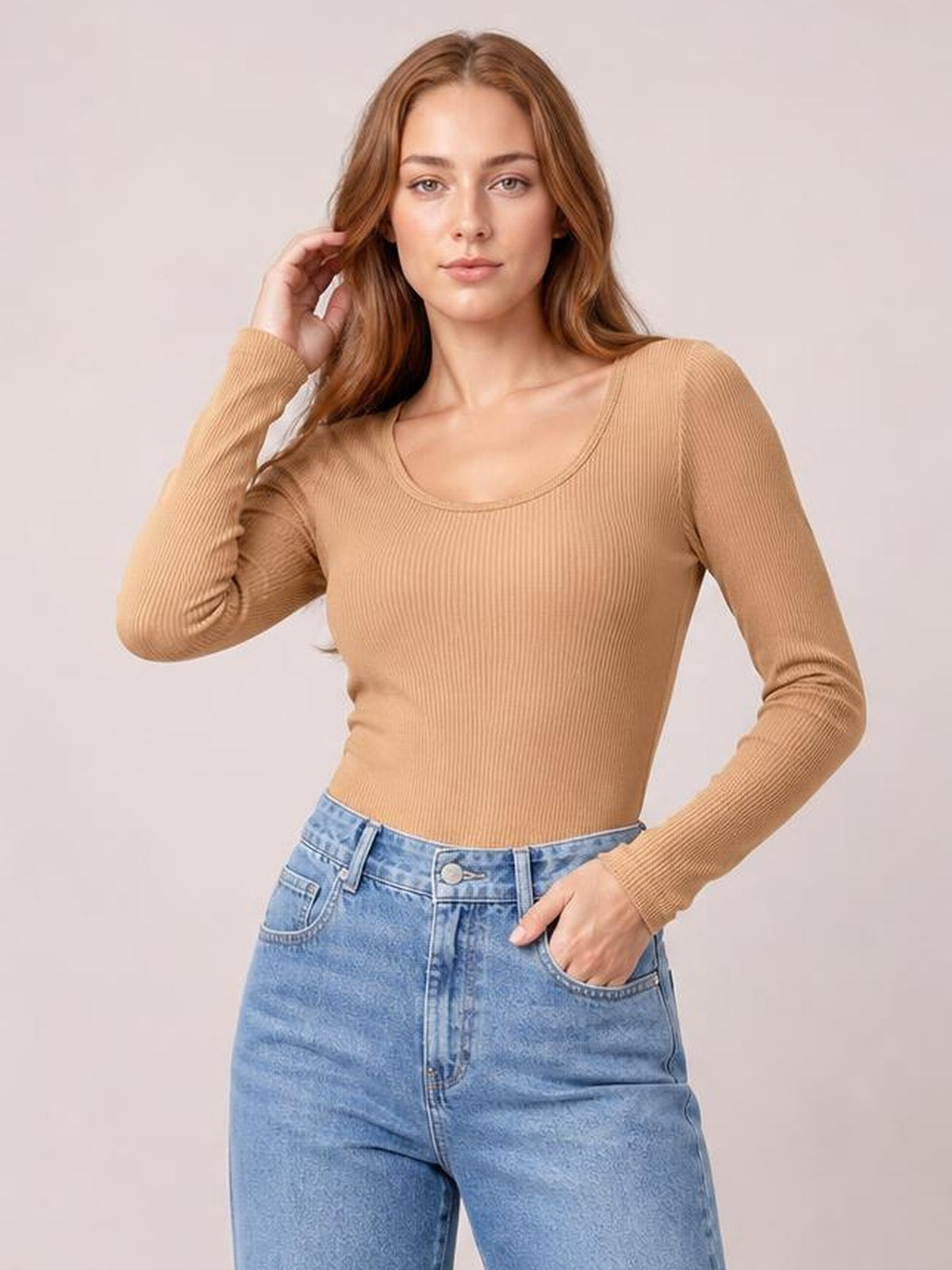 Model poses in a fitted camel long sleeve scoop neck T-shirt with ribbed construction, tucked into light-wash jeans.