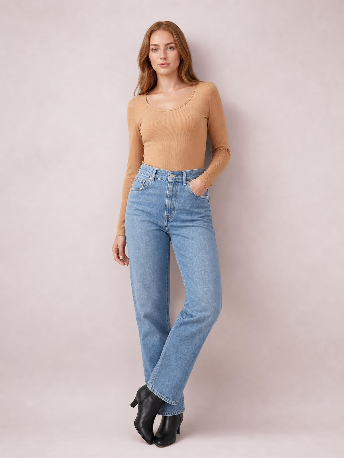 Model poses in a camel long sleeve scoop neck T-shirt with a fitted silhouette, ribbed construction, and one hand in her jeans pocket.