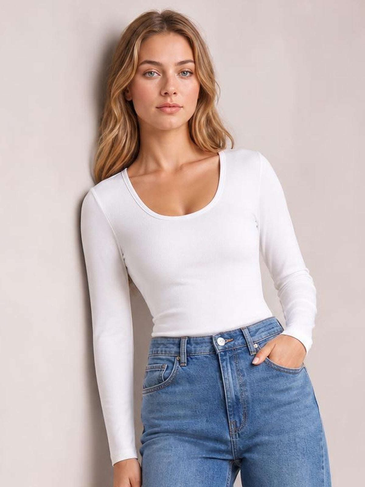 Model in a white long sleeve scoop neck T-shirt with a fitted silhouette, standing with one hand in her jeans pocket.