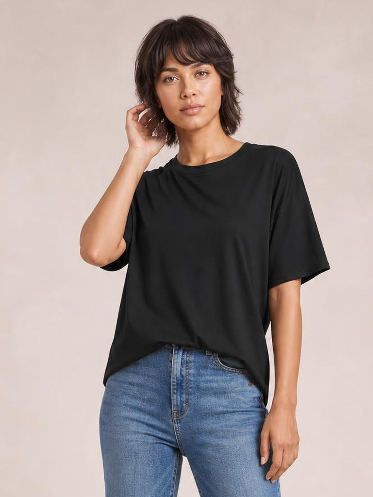 Model poses in a black exposed seam round neck half sleeve T-shirt with a relaxed silhouette, paired with blue jeans.